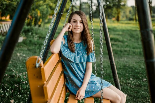 Young woman relaxing on wooden swing in summer park