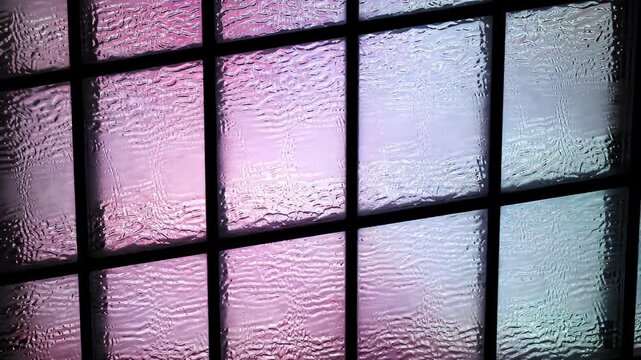 Distorted aqua light shines through textured window panes divided by dark framing
