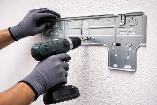 Closeup of technician using a power drill to install a metal mounting bracket for a wall mounted air conditioner. Concept of HVAC installation, home improvement, and technical service work.