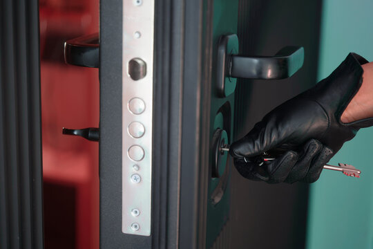 Person in black leather glove unlocking residential door with keys. Concept of theft, break‑in, hidden identity, illegal access to property, squatter intrusion and tense unknown entry. Photo