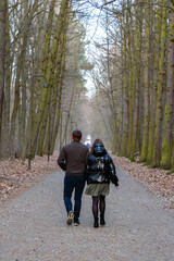Obraz premium Rear view of a middle-aged couple walking together along a gravel path lined with lanterns in a peaceful autumn forest park during the daytime.