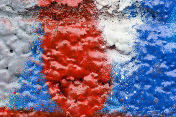 Macro close-up of a uneven wall spray painted in red, blue, white and gray. Abstract full frame textured splattered graffiti background with copy space.
