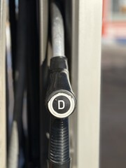 Closeup gas pump nozzles lined vertically, worn plastic handles with red yellow and black caps, coiled hoses and metal dispenser © vipvn