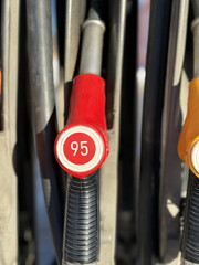 Closeup gas pump nozzles lined vertically, worn plastic handles with red yellow and black caps, coiled hoses and metal dispenser © vipvn