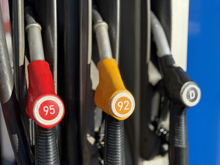 Closeup gas pump nozzles lined vertically, worn plastic handles with red yellow and black caps, coiled hoses and metal dispenser © vipvn
