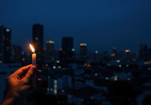 A hand holding a lit candle in a calm, reflective mood against a dark city skyline, symbolizing Earth Hour and the spirit of unity during the blackout