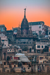 Fototapeta premium Historic temple structure with intricate carvings and spires, surrounded by traditional buildings along the riverbank at sunset in Varanasi, India, showcasing cultural heritage 