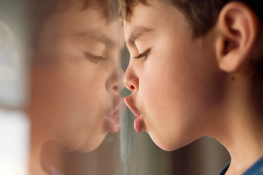 Close-up side view of a Boy's face pressed against a window pulling funny faces