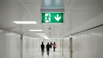 Fototapeta premium An illuminated green exit sign directs people down a sterile, modern hallway.