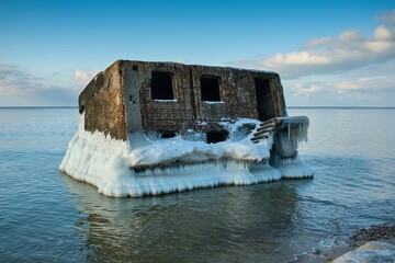 Historic concrete fort ruins in the frozen Baltic Sea covered with thick ice and icicles. Abandoned WWII bunker in winter coastal landscape of Liepaja, Latvia. Cold arctic scenery under blue sky. © Igor