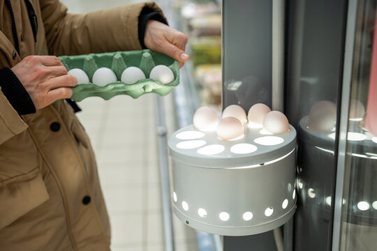 Unrecognizable female customer checking raw eggs contents in ovoscope device, using special station for candling product and detect defects inside egg, helpful method for fresh and healthy eating.