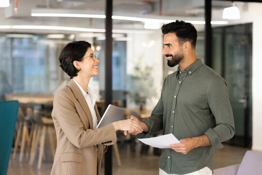 Two multiethnic businesspeople shake hands in office. HR manager greeting applicant, starts job interview, successful deal closure, partnership, and mutual agreement after productive business meeting