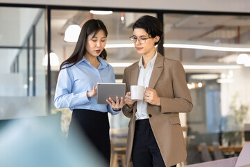 Two focused multiethnic businesswomen engaged in professional collaboration, reviewing data and...