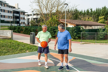 Obraz premium Two active senior men are enjoying a friendly game of basketball on an outdoor court, demonstrating healthy wellbeing and continuing sport life in their old age
