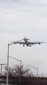 A giant white 4 engine 747 airplane coming in for a landing over a bridge.