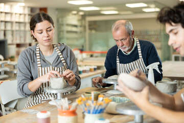 Fototapeta premium During working day, three pottery workshop workers sculpt from raw clay, form final product