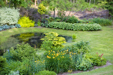 Fototapeta premium Lush garden with vibrant flowers and a tranquil pond surrounded by greenery in early summer
