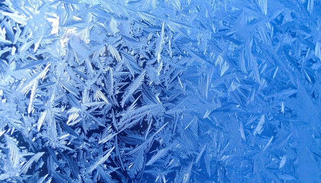 Close-up of blue frosty glass covered with sharp, sparkling ice crystal patterns. 