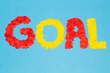 Text “goal” formed with red and yellow confetti on a blue background with a wide horizontal composition, concept of celebrating a soccer goal © Andres Serna