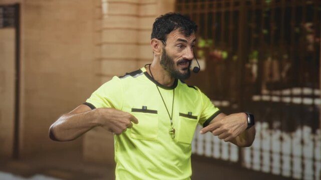 Man points finger to chest wearing neon yellow tshirt with whistle on lanyard in building, headset mic and smartwatch visible; team leadership assertive.