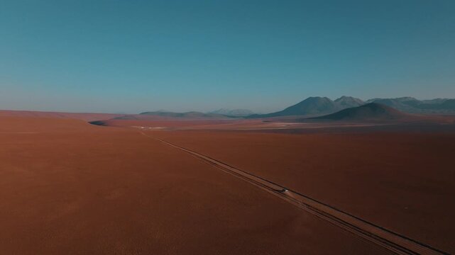 Aerial view of a car traveling through the vast landscapes of northern Chile. Desert plains and volcanic mountains stretch across the horizon.