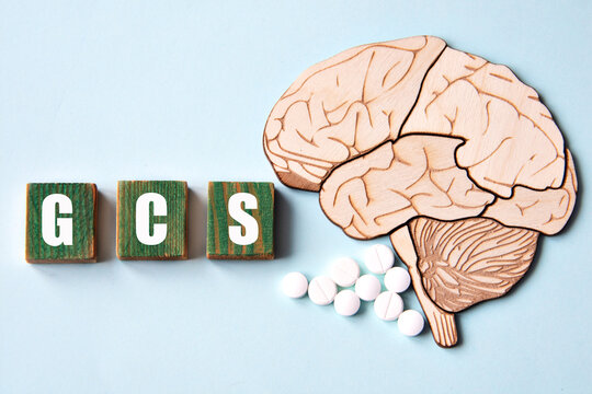 GCS is an acronym depicted on wooden cubes on a blue background with a skull brain model.