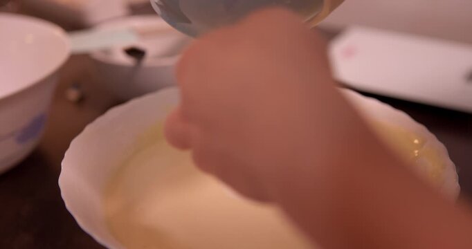 Baking Process: A close-up view capturing the precise moment of a hand pouring a creamy mixture into a white bowl, a culinary journey unfolding.