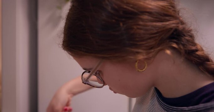 Focused Concentration: A young woman with auburn hair is deeply engrossed in her task, her gaze fixated as she meticulously works.
