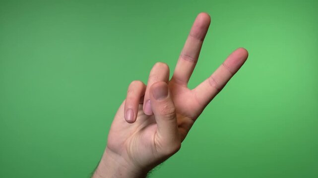 Close up video of a hand showing the peace symbol with first two fingers raised against a solid green background.