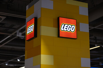 Naklejka premium Wroclaw, Poland- October 25, 2025: Lego store logo and illuminated brand signage mounted on a yellow brick patterned column inside a modern retail shopping mall for family entertainment