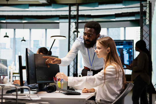 Lead programmer providing support to new worker using PC in software development agency. African american IT expert helping trainee coding during internship in tech startup