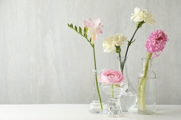 Different beautiful flowers in vases on light table indoors. Space for text