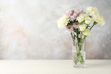 Beautiful flowers in vase on light table indoors. Space for text