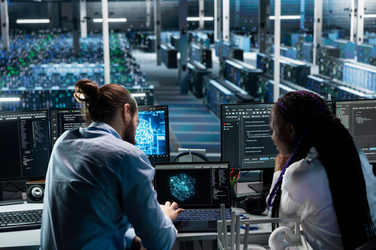 Server hub team leader helping intern optimize supercomputers performance with AI assistant analysis. Data center manager and young woman using LLM chatbot suggestions to speed up tasks