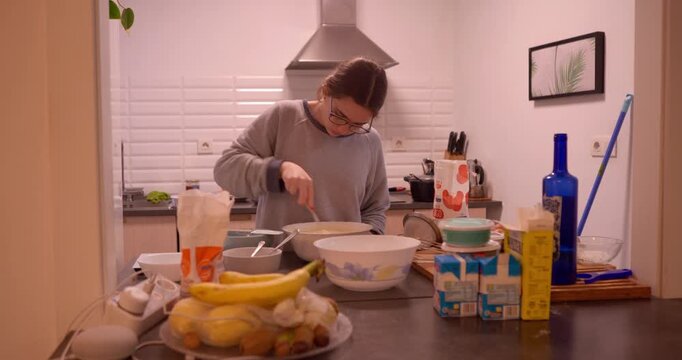 Baking Morning: A person in a domestic kitchen carefully prepares ingredients for cooking, stirring a bowl with focused attention. Capturing a simple morning and culinary activity.