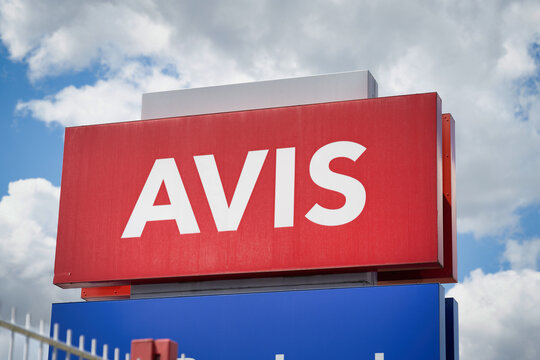 Cologne, Germany July 15 2025: Red and white Avis car rental logo sign against a bright, cloudy sky. Editorial shot of a corporate brand identity in an urban setting