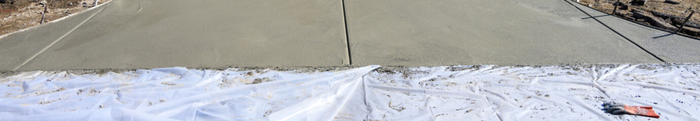 New home construction, housing supply, freshly poured wet concrete driveway and front patio, sunny day on new neighborhood development winter job site
