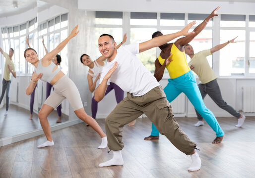 European guy teaches sequences of movements, actions during dance lesson, trains to doing elements of RnB dance, enjoys active hobby to music. Multinational group rehearsal, dance choreography coach
