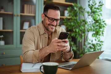 Happy man using smart phone while working remotely from home