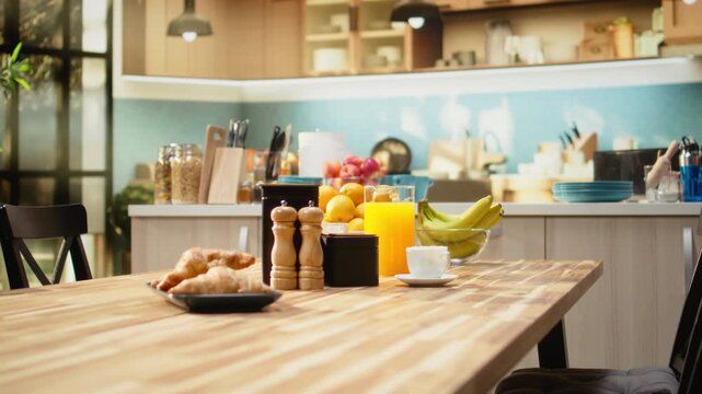 Kitchen interior with croissants and coffee for breakfast meal. Warm tones and natural light in empty home interior. Wooden table and kitchenware creates modern atmosphere with no people indoors.