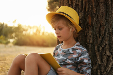 Fototapeta premium Cute little boy reading book near tree in park