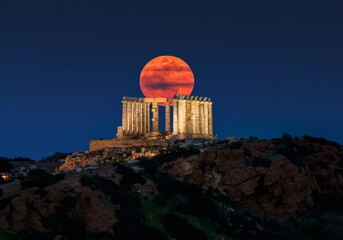 Naklejka premium Red moon, or Blood moon, rise behind the ancient Tempel of Poseidon in Sounion, Attica, Greece