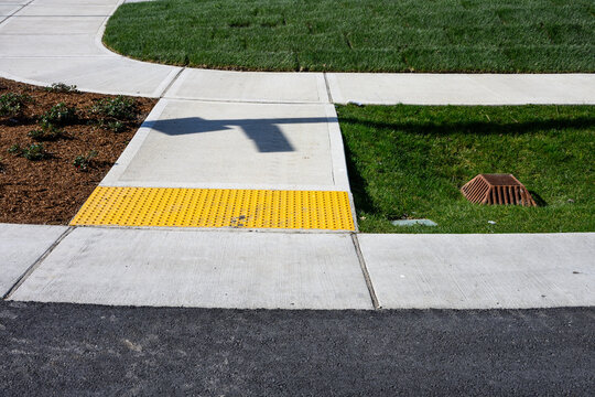 Freshly installed concrete sidewalk, yellow ADA Curb Ramp, and landscaping in new residential neighborhood development on sunny winter day
