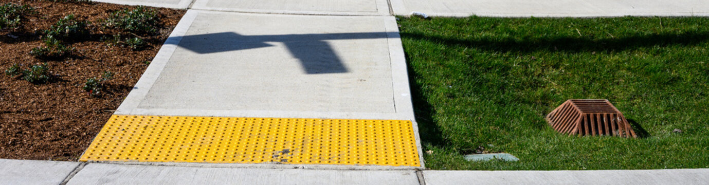 Freshly installed concrete sidewalk, yellow ADA Curb Ramp, and landscaping in new residential neighborhood development on sunny winter day
