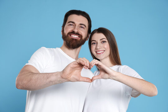 Romantic date. Lovely couple making heart with hands on light blue background