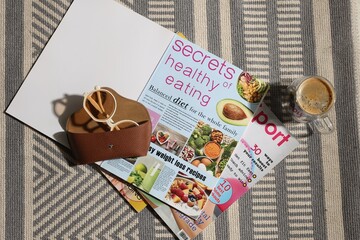 Lifestyle magazines, glasses and cup of coffee on rug indoors, flat lay