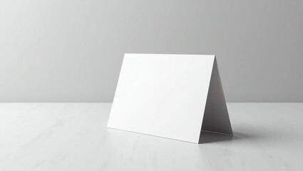 Naklejka premium blank white folded brochure or greeting card standing upright in a tent position on a light gray textured surface