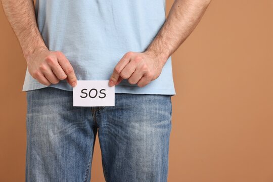 Urology. Man holding note with word SOS on beige background, closeup. Space for text