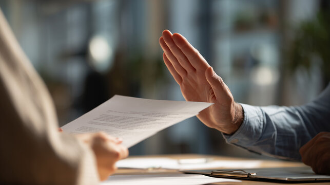 A business professional makes a definitive stop gesture, rejecting documents presented by a colleague during a serious discussion.