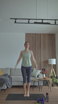 Woman doing jumping exercise on mat with dumbbells and water bottle nearby